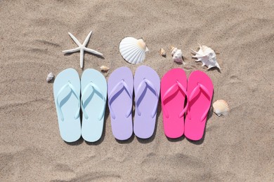 Stylish colorful flip flops, starfish and seashells on sand outdoors, flat lay