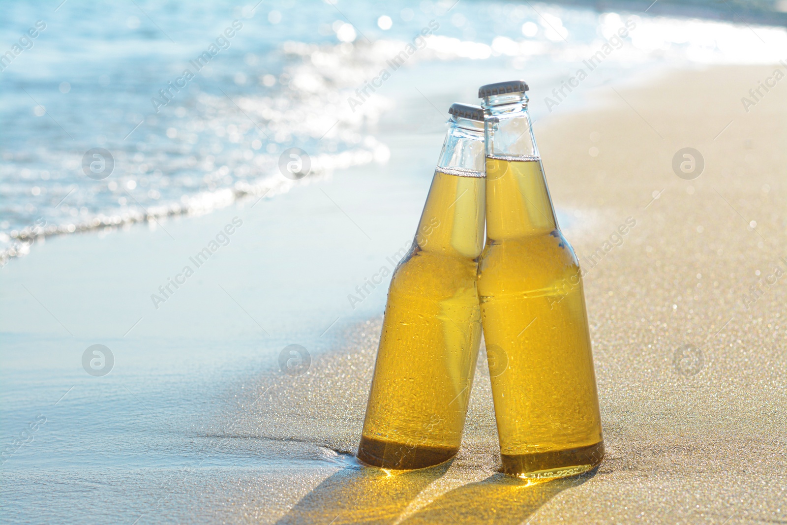 Photo of Bottles of cold beer on sandy beach near sea, space for text