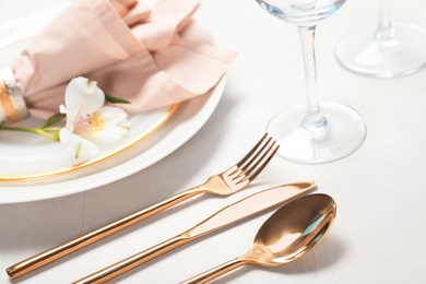 Photo of Golden cutlery and plates with napkin on light background, closeup. Festive table setting