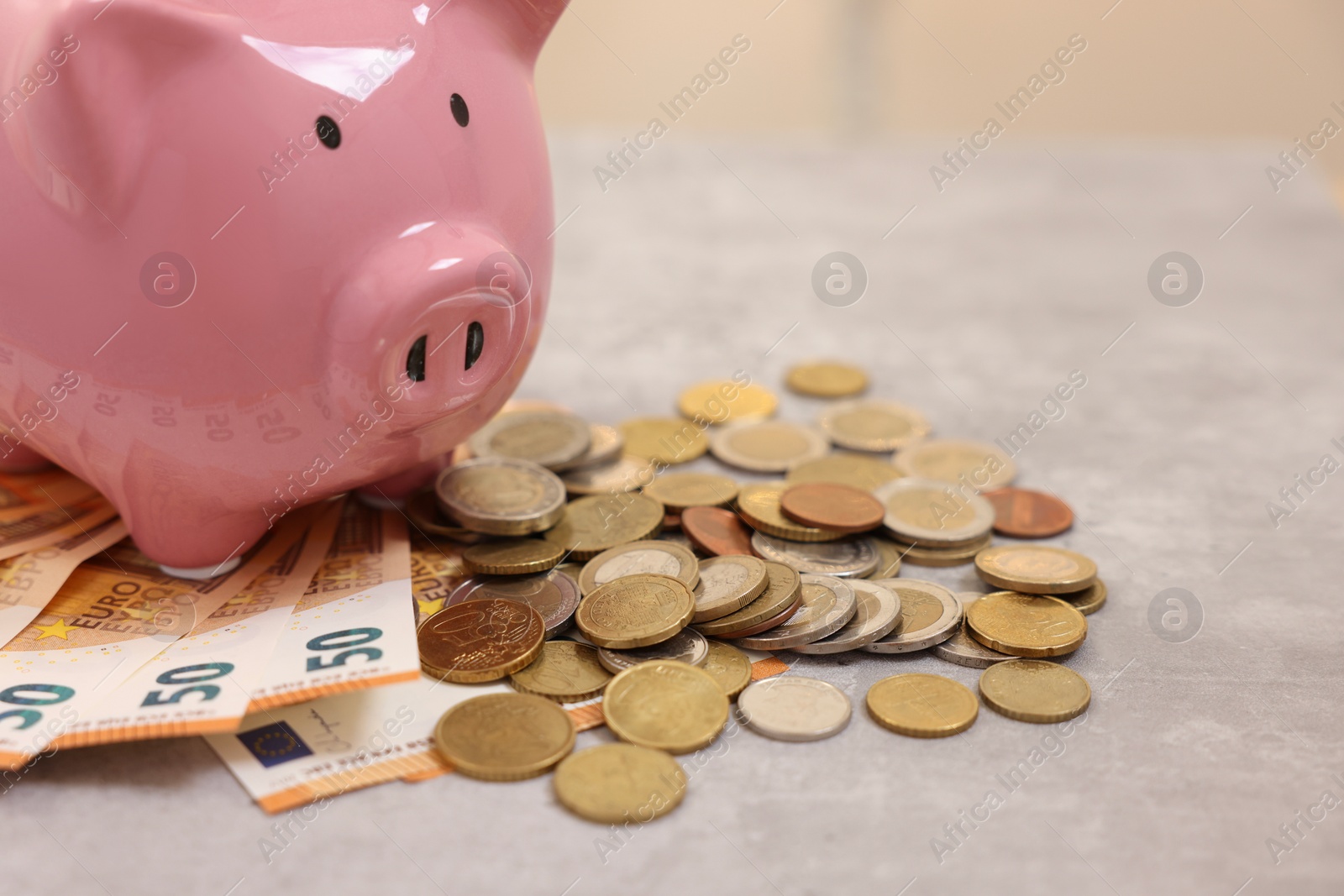 Photo of Piggy bank with euro banknotes and coins on grey table, closeup