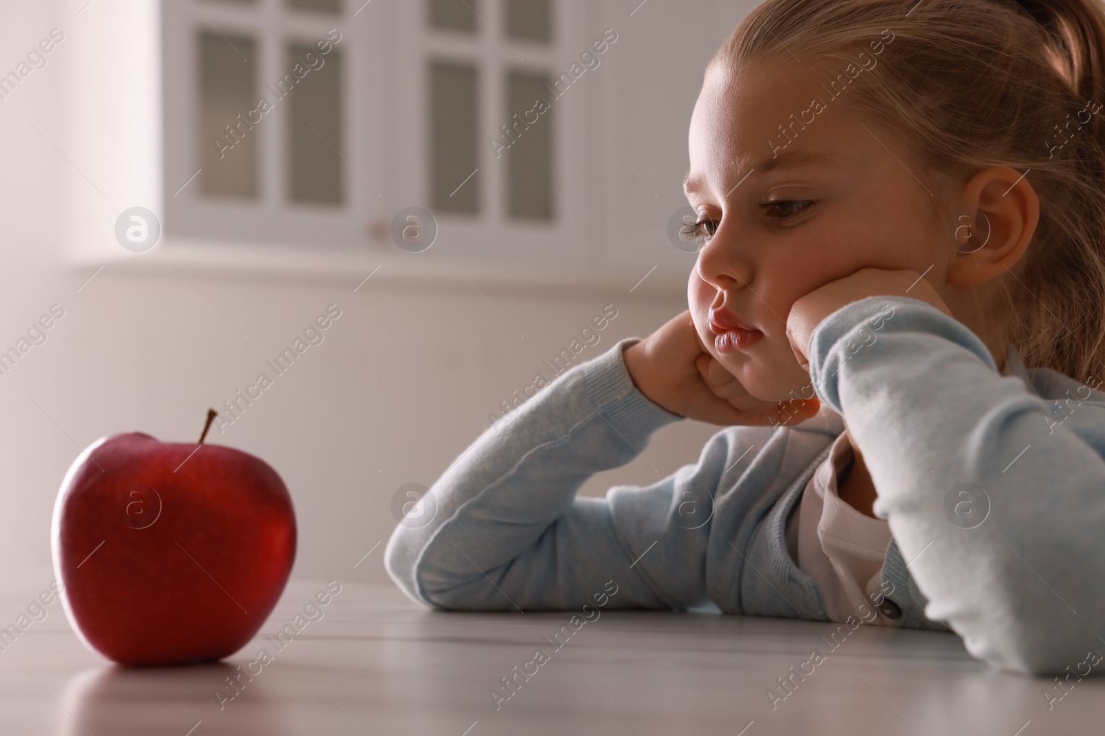 Photo of Cute little girl refusing to eat apple in kitchen