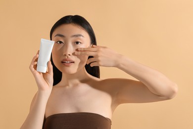 Photo of Beautiful young woman holding sun protection cream on beige background, space for text