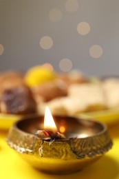 Photo of Happy Diwali. Diya lamp on yellow table against blurred lights, closeup. Space for text