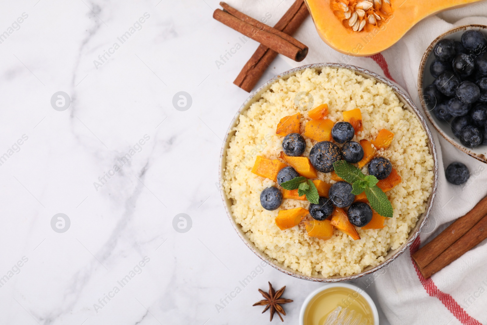 Photo of Bowl of tasty couscous with blueberries, pumpkin, ingredients on white marble table, flat lay. Space for text