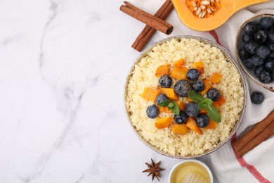 Photo of Bowl of tasty couscous with blueberries, pumpkin, ingredients on white marble table, flat lay. Space for text