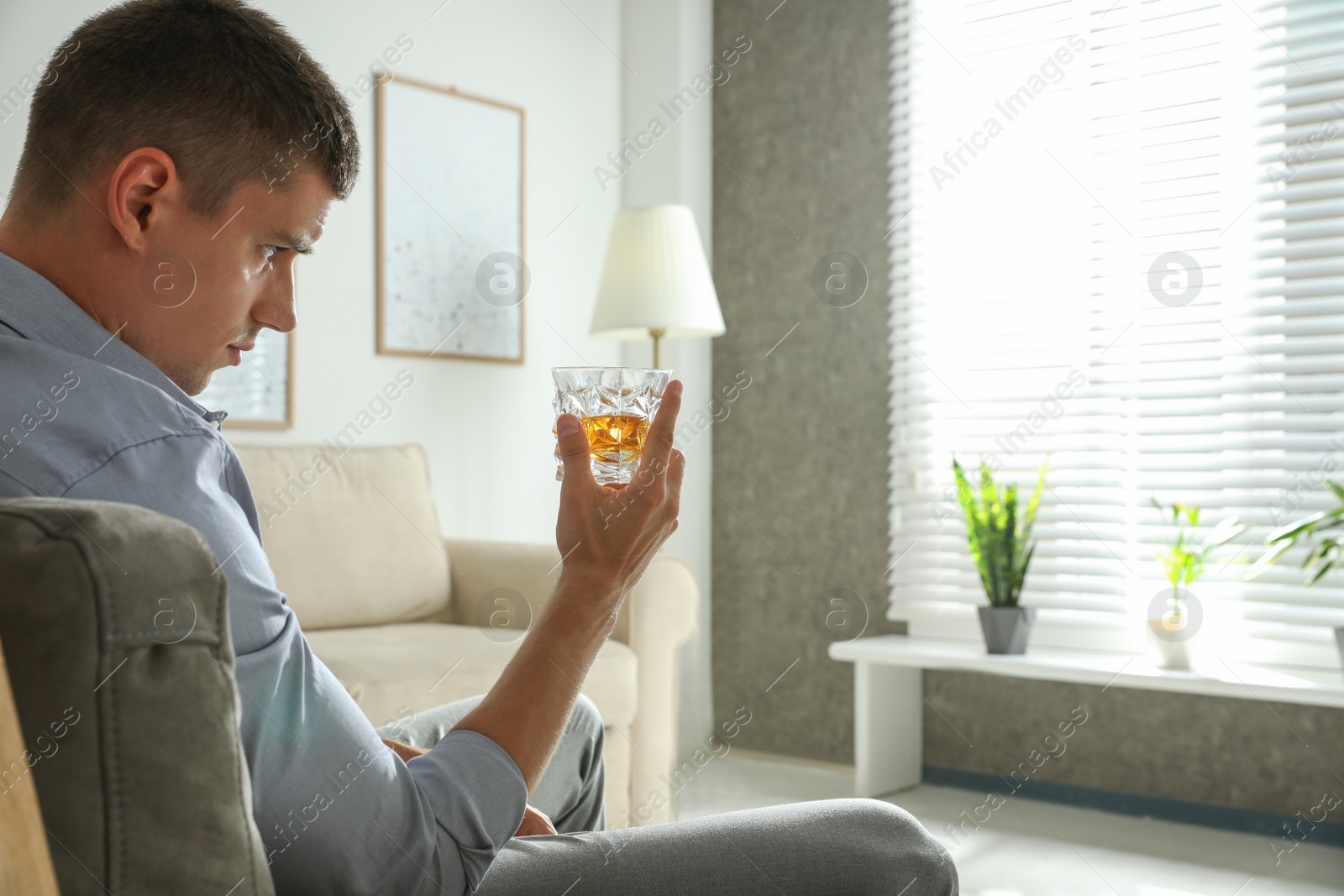 Photo of Young man with glass of whiskey at home. Space for text