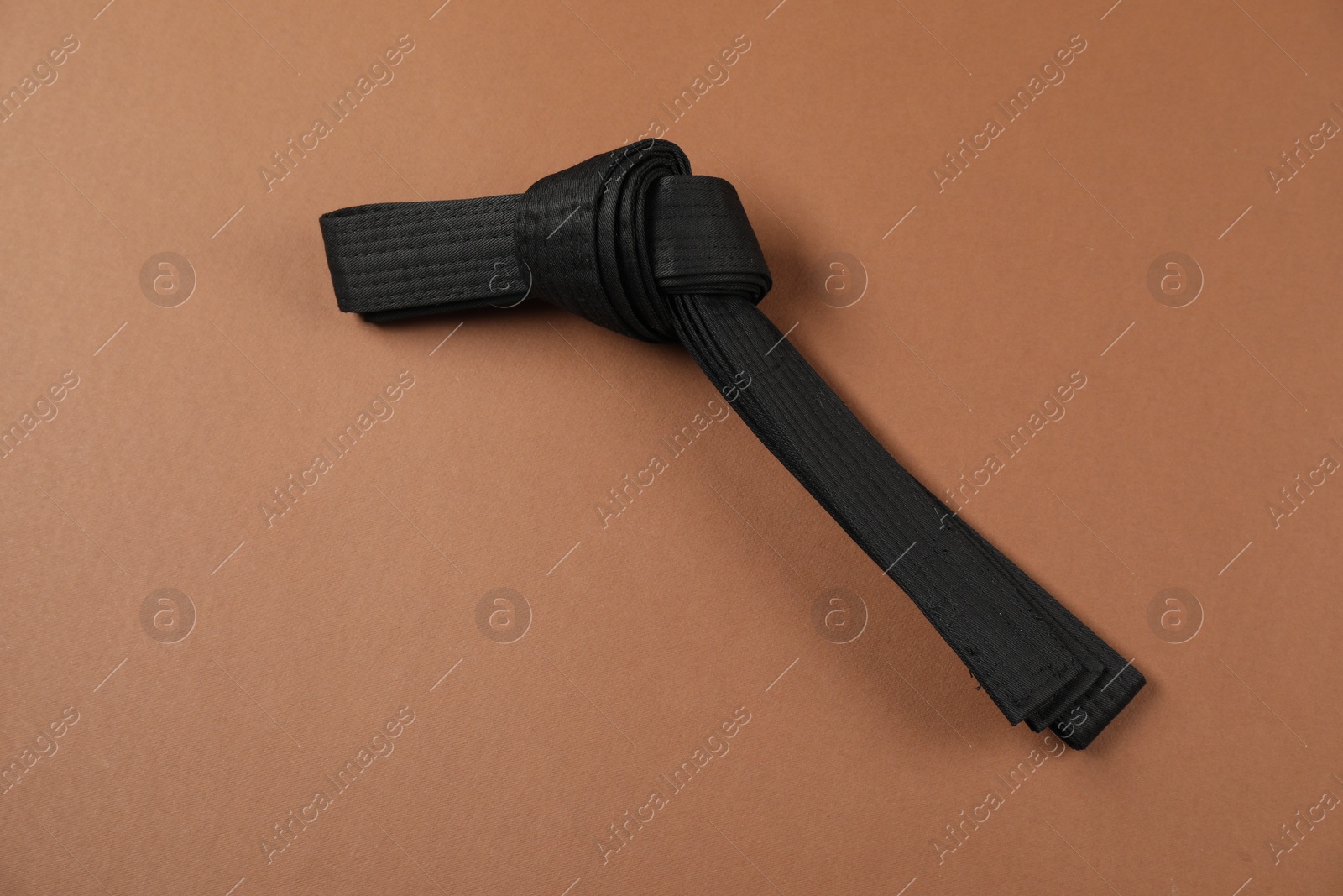 Photo of Black karate belt on brown background, top view. Space for text