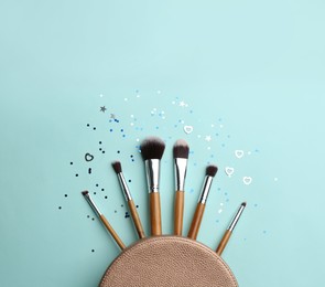 Different makeup brushes, case and shiny confetti on turquoise background, flat lay