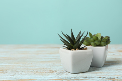 Photo of Artificial plants in white flower pots on light blue wooden table. Space for text