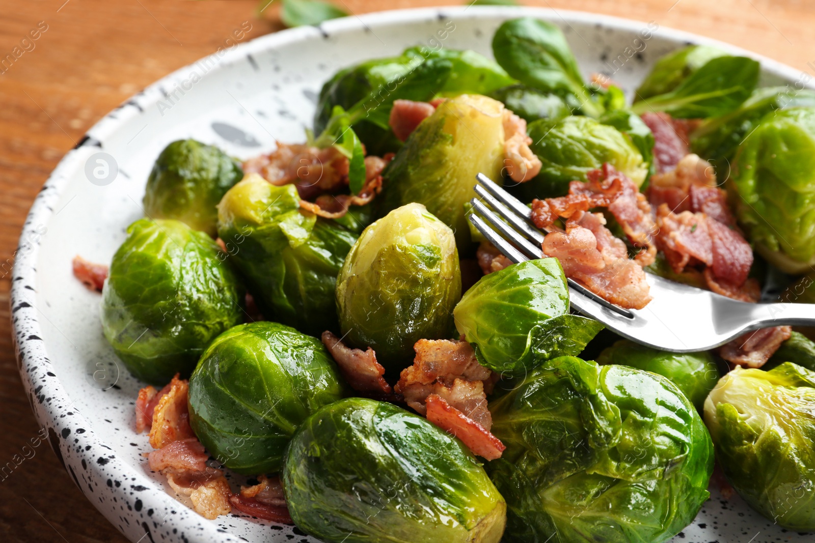 Photo of Tasty roasted Brussels sprouts with bacon on wooden table, closeup