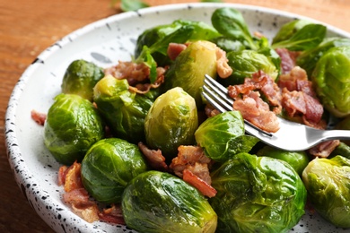 Photo of Tasty roasted Brussels sprouts with bacon on wooden table, closeup