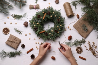 Florist making beautiful Christmas wreath at white wooden table, top view