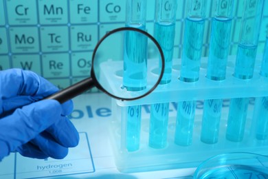 Scientist with magnifying glass examining test tube against periodic table of elements in laboratory, closeup. Color tone effect