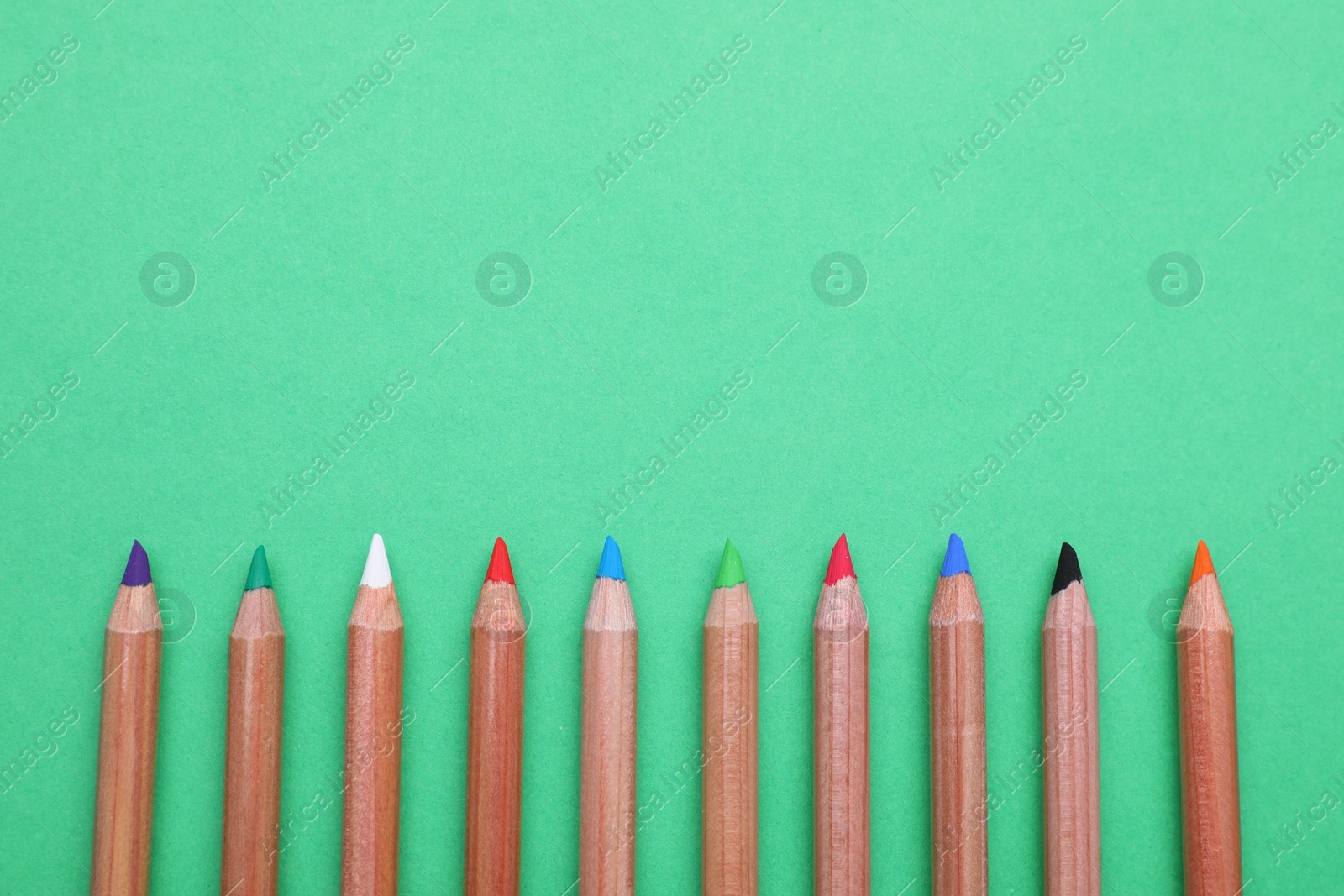 Photo of Many colorful pastel pencils on light green background, flat lay and space for text. Drawing supplies