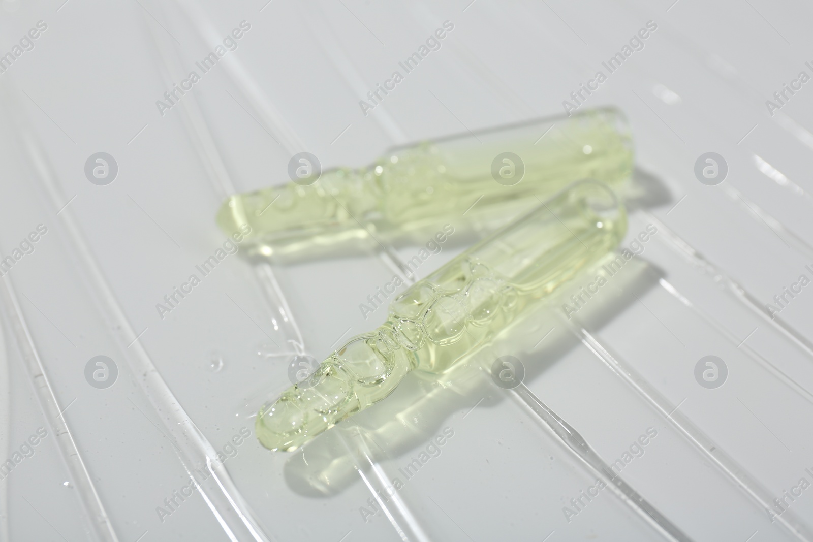 Photo of Skincare ampoules on white surface covered with gel, closeup