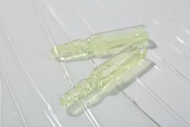 Photo of Skincare ampoules on white surface covered with gel, closeup