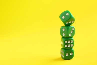 Photo of Many stacked green game dices on yellow background, closeup. Space for text