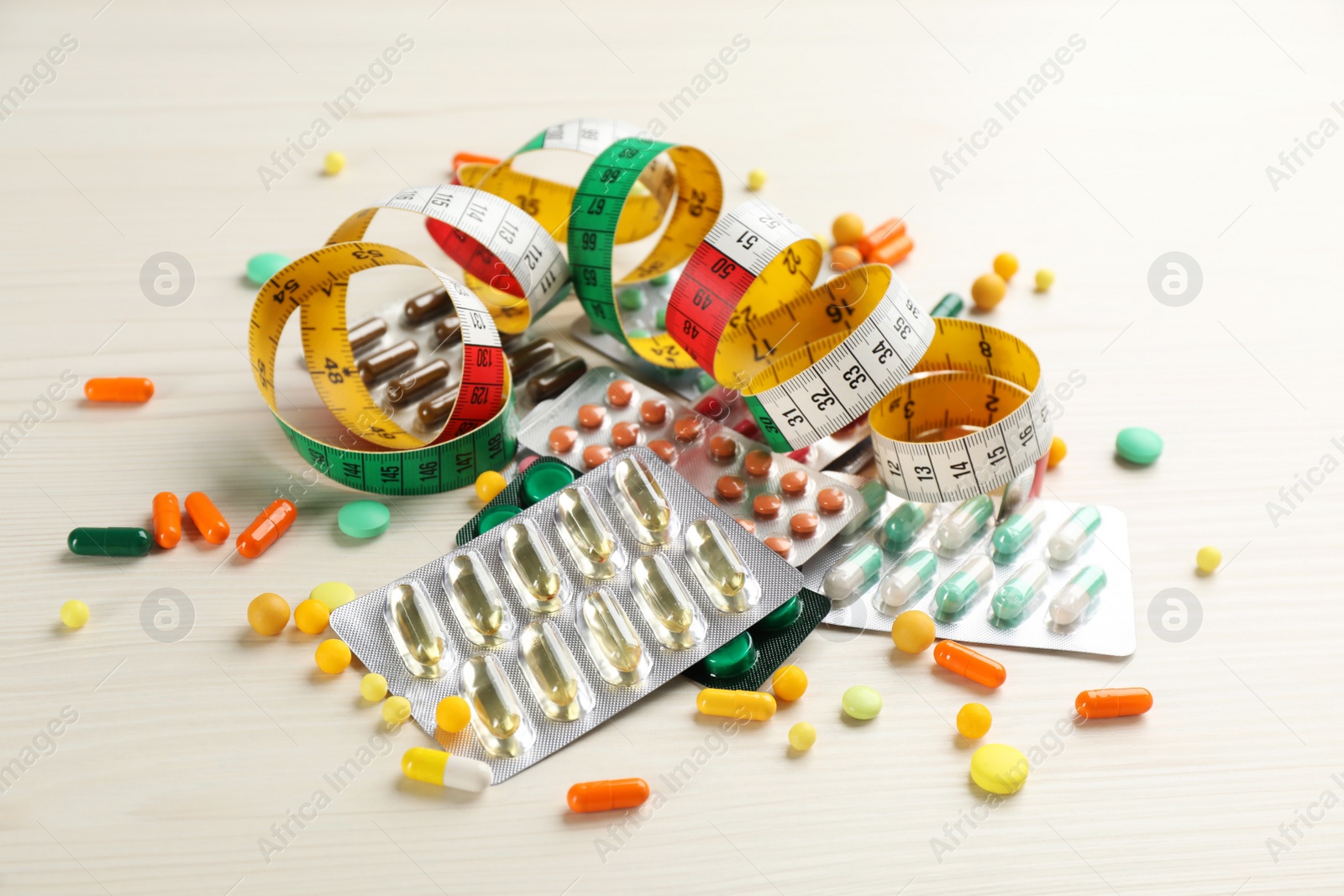 Photo of Many different weight loss pills and measuring tape on white wooden table