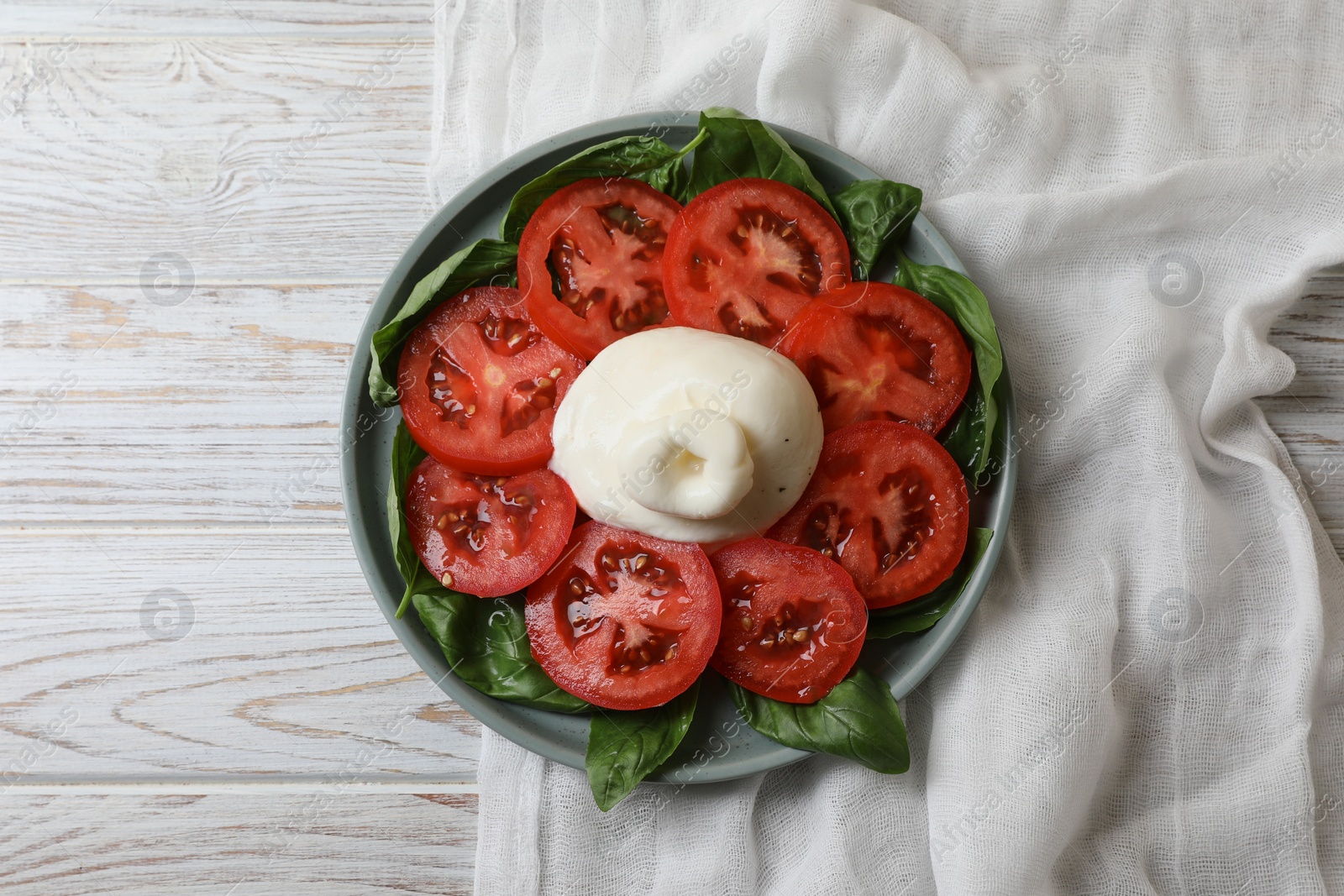 Photo of Delicious burrata cheese with tomatoes and basil on white wooden table, top view