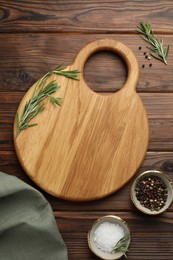 Photo of Cutting board, salt, pepper and rosemary on wooden table, flat lay. Space for text