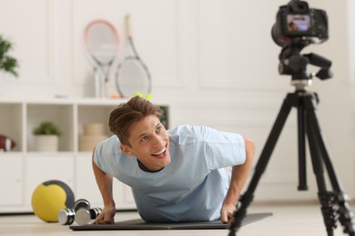 Photo of Smiling sports blogger doing push-ups while recording fitness lesson with camera at home