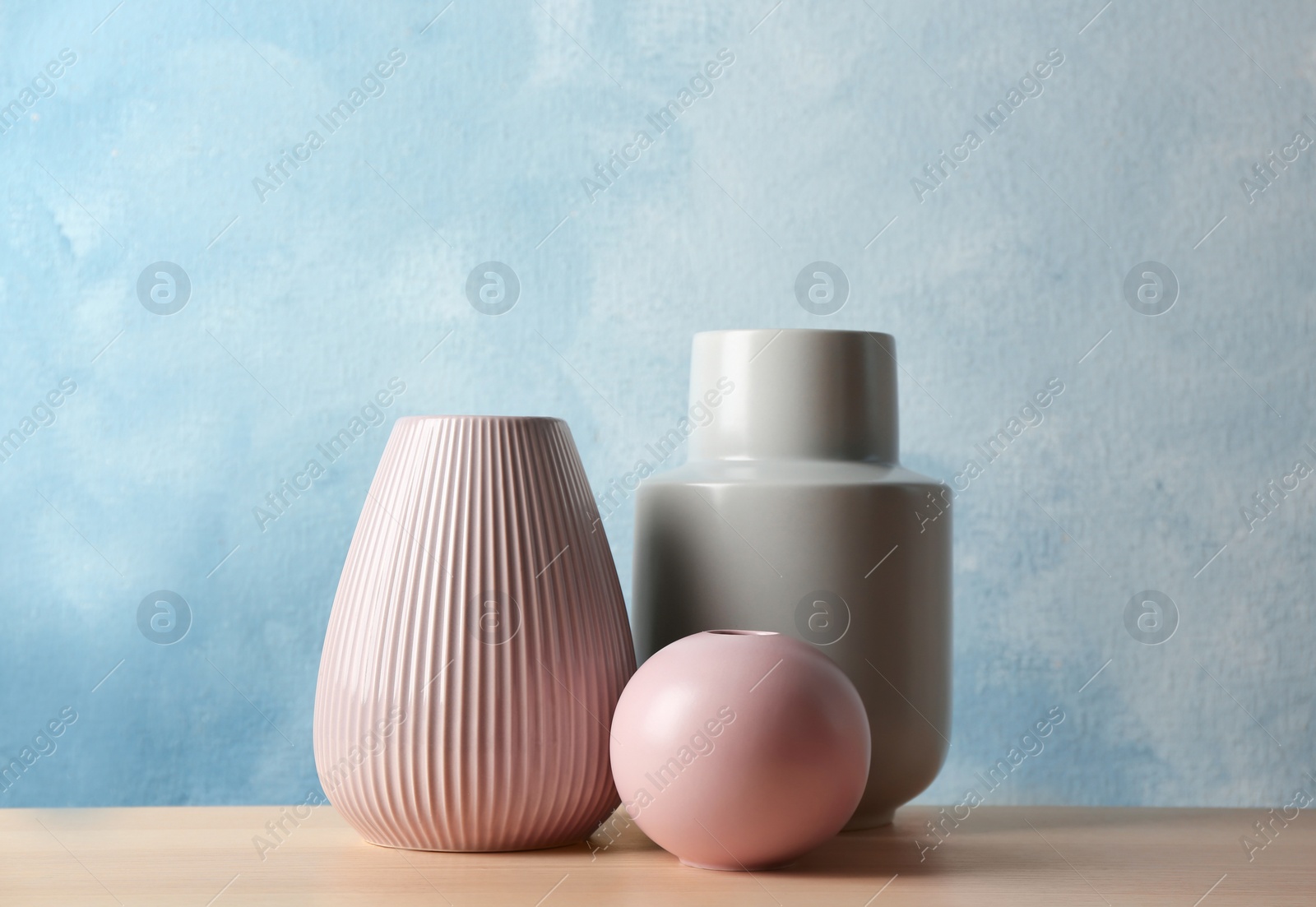 Photo of Stylish ceramic vases on wooden table against light blue background