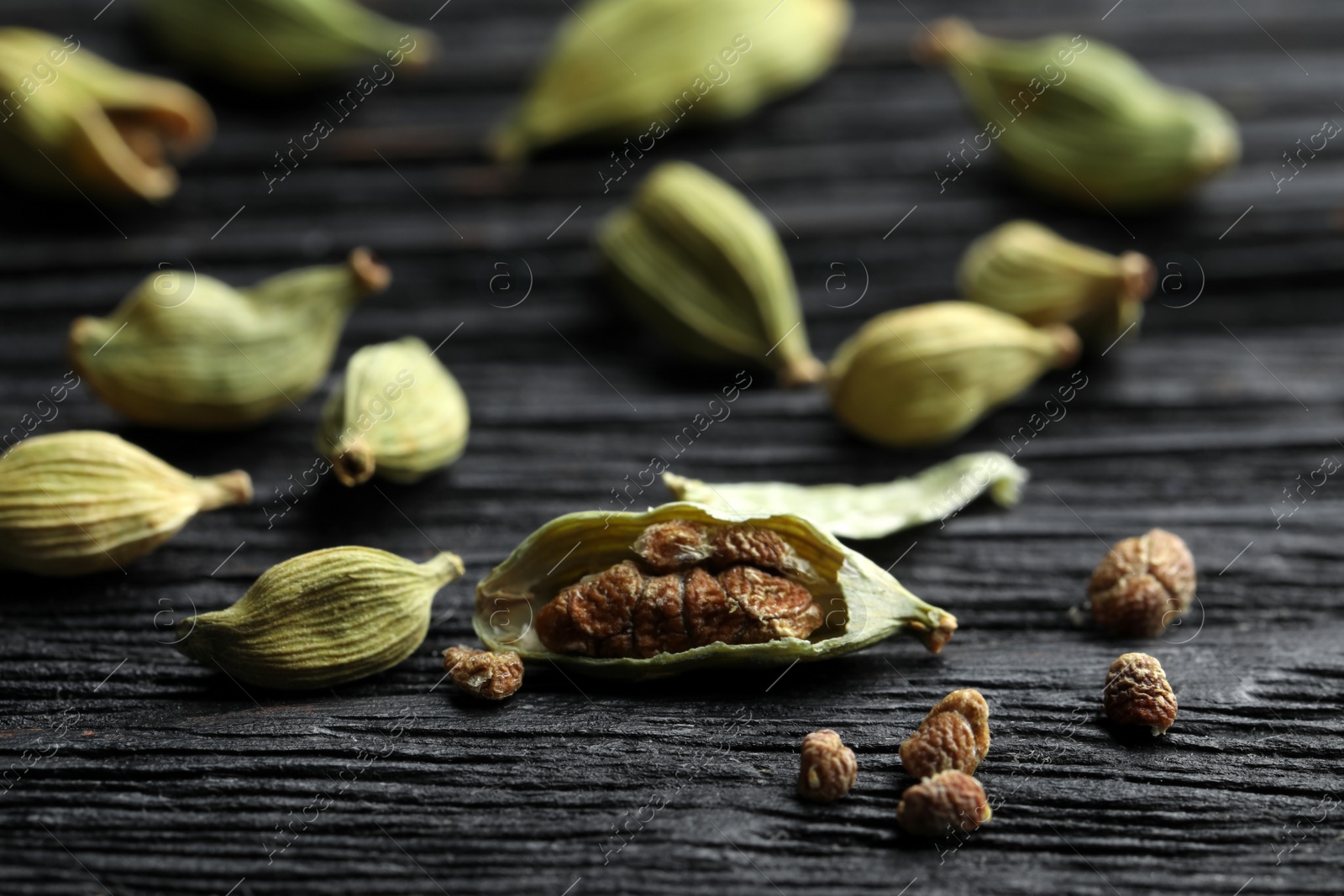 Photo of Dry cardamom pods on black wooden table, closeup