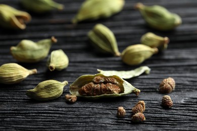 Dry cardamom pods on black wooden table, closeup