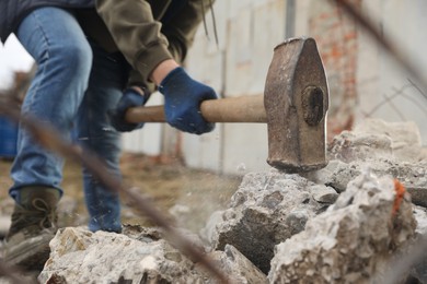 Photo of Man breaking stones with sledgehammer outdoors, closeup