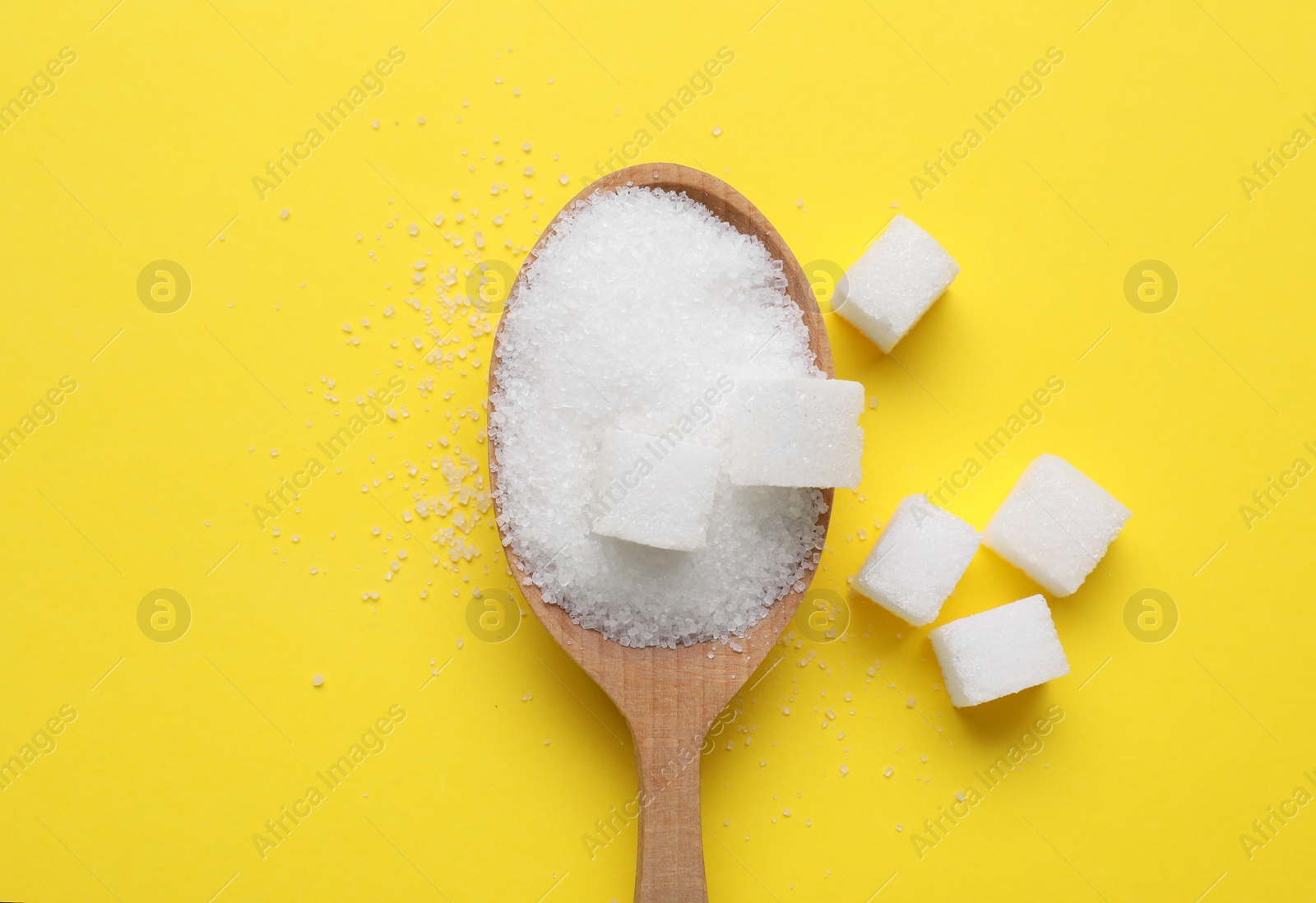 Photo of Spoon with refined and granulated white sugar on yellow background, flat lay