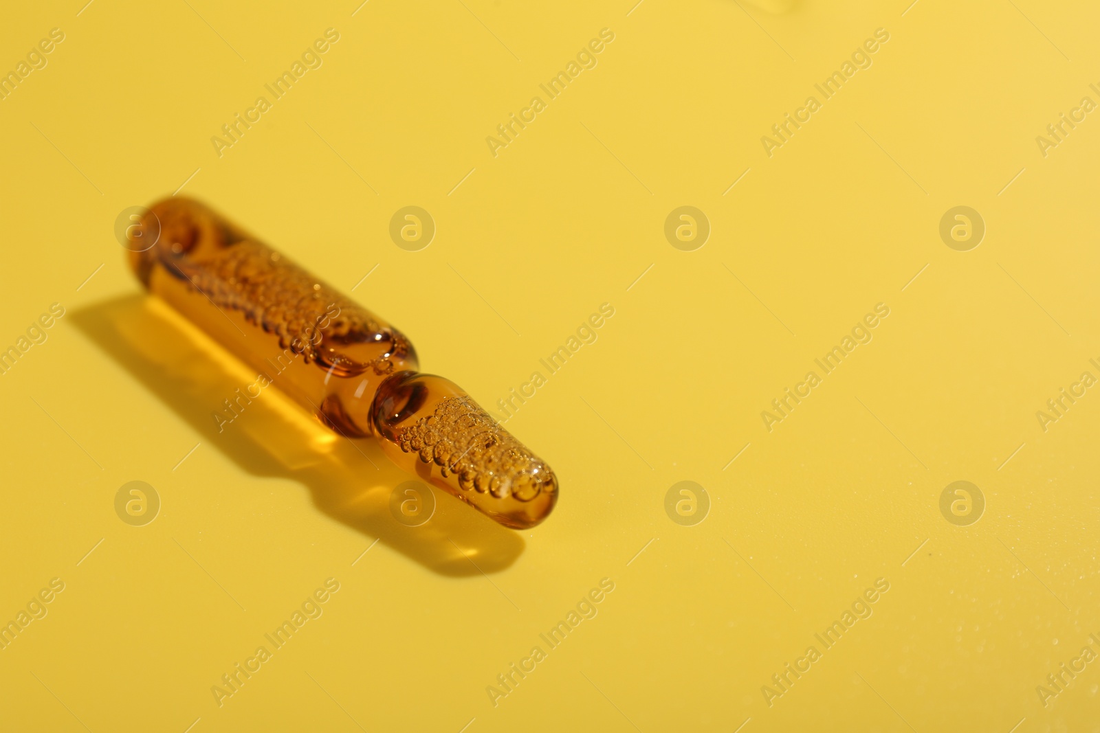 Photo of Glass ampoule with liquid on yellow background, closeup. Space for text