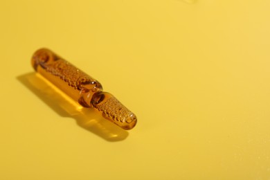 Glass ampoule with liquid on yellow background, closeup. Space for text