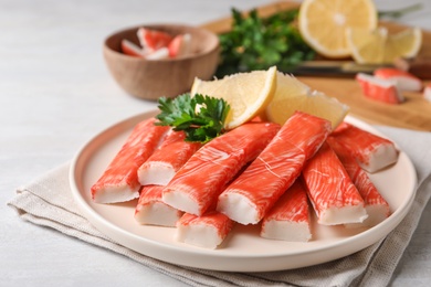 Photo of Plate of fresh crab sticks with lemon on white table, closeup