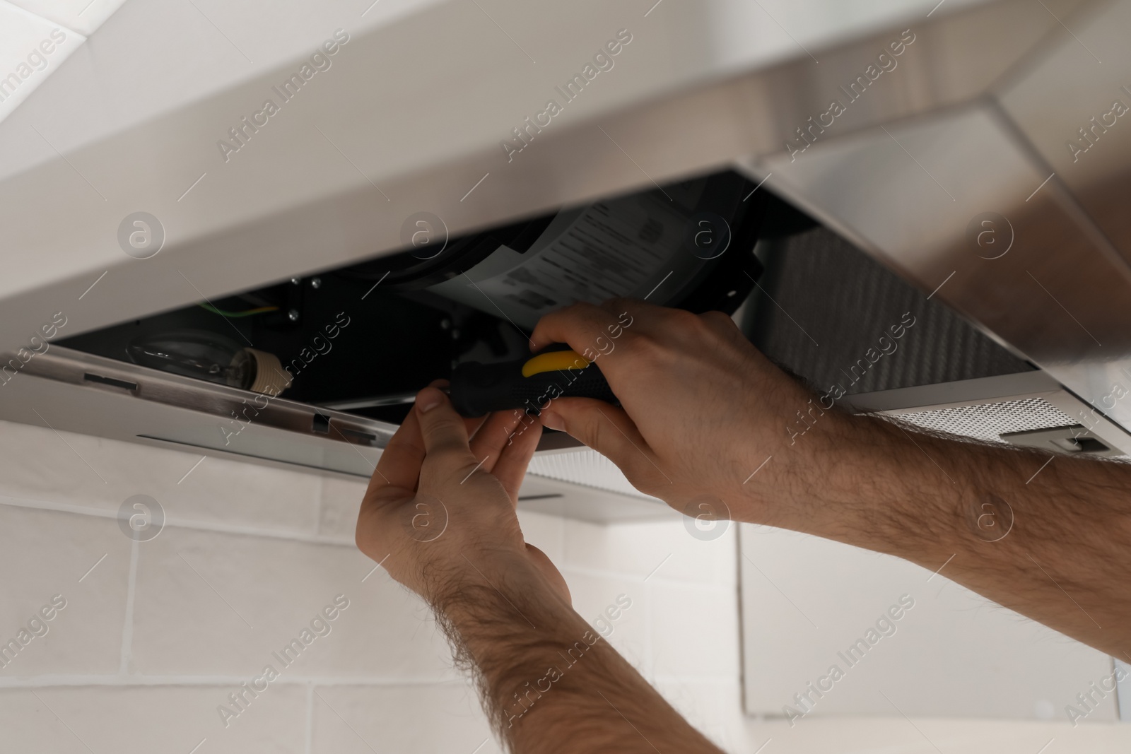 Photo of Worker repairing modern cooker hood indoors, closeup