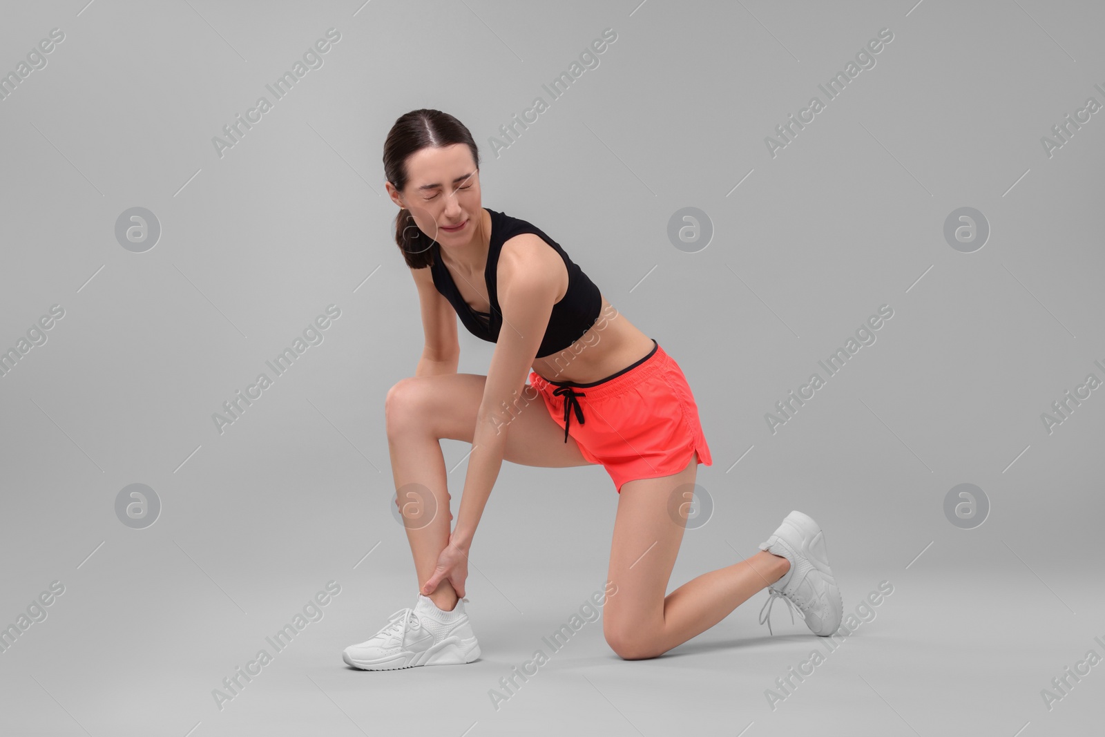 Photo of Young woman suffering from leg pain on grey background