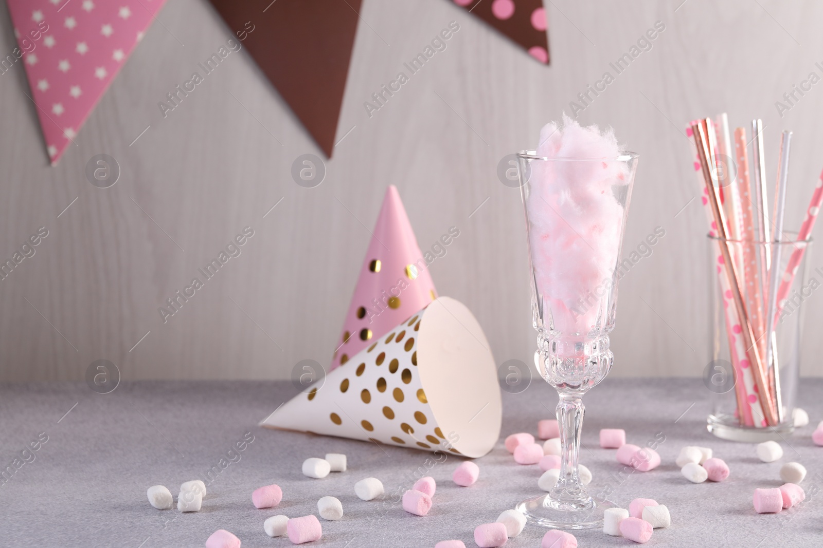 Photo of Tasty cotton candy cocktail in glass, festive decor and marshmallows on gray table against light wooden wall