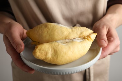 Photo of Woman holding plate with pieces of durian on light background, closeup