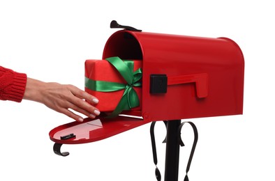 Woman putting Christmas gift into mailbox on white background, closeup. Sending present by mail