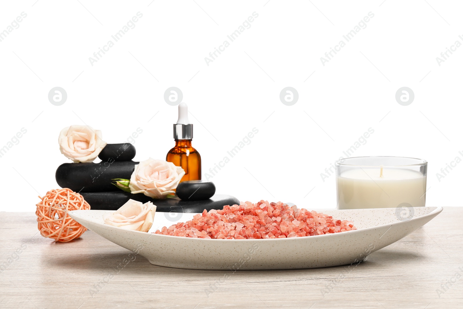 Photo of Natural sea salt in bowl and other spa supplies on wooden table against white background