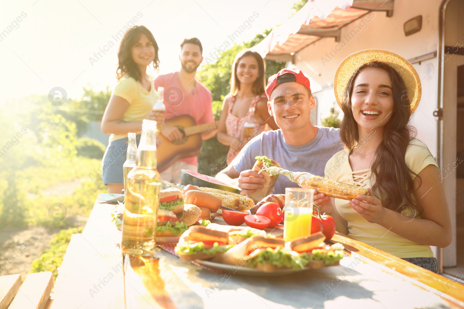 Photo of Happy friends with drinks and food near motorhome. Camping season