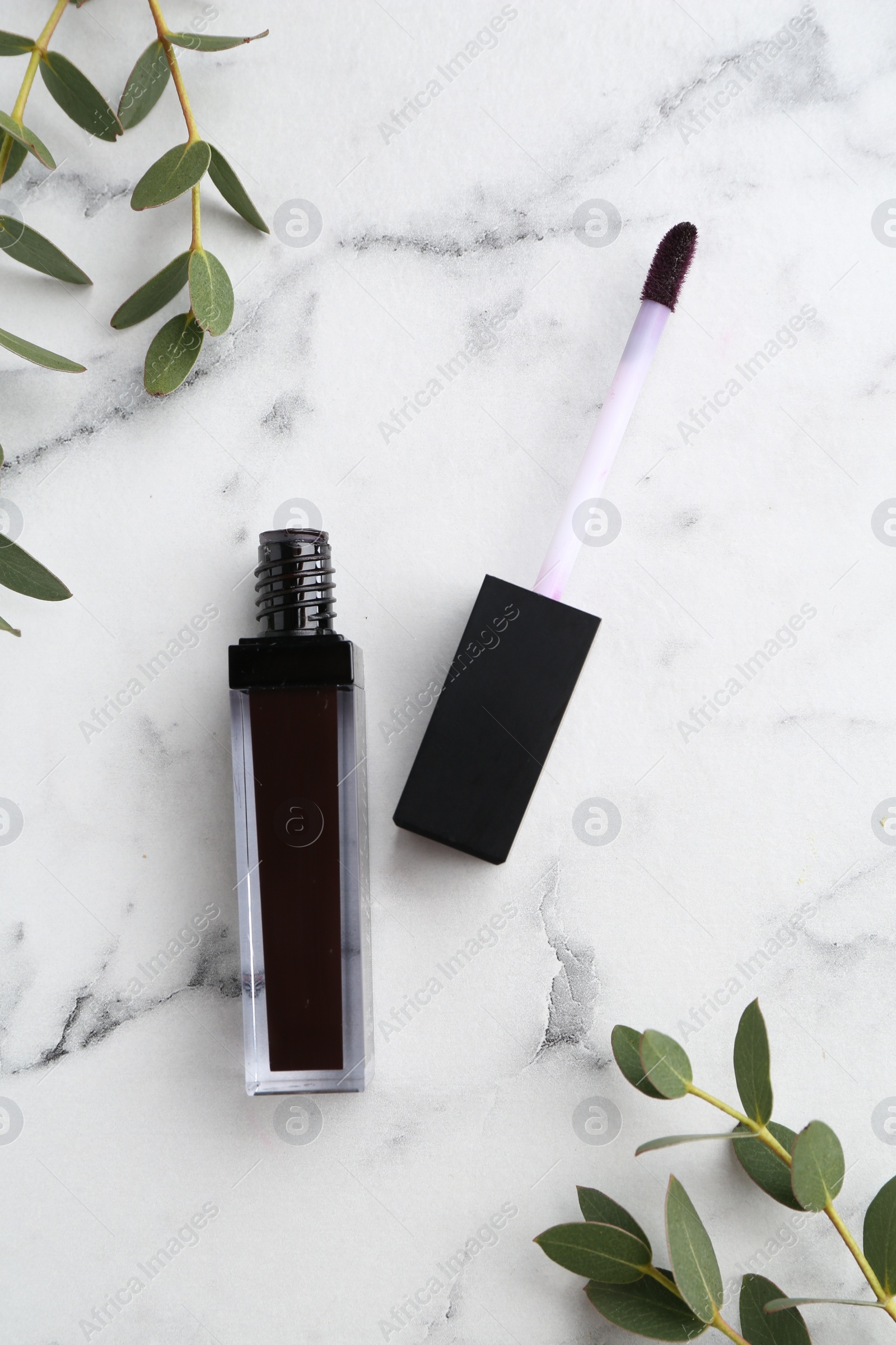 Photo of Purple lip gloss, applicator and green leaves on white marble table, flat lay