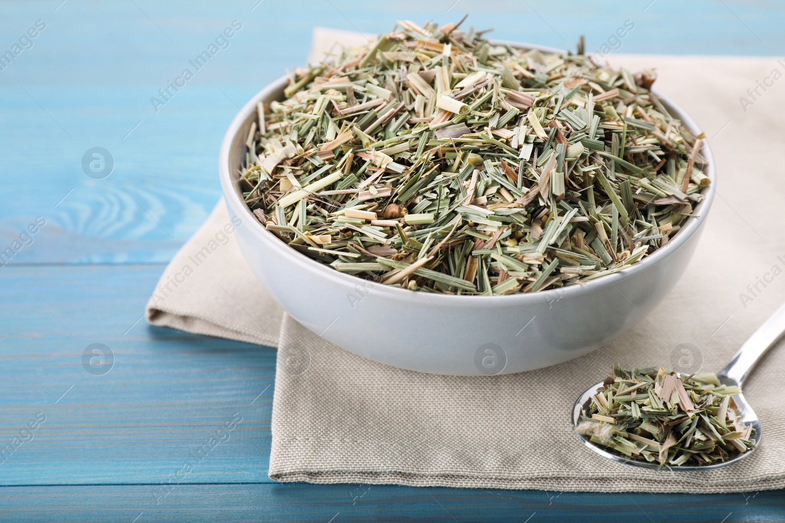 Photo of Bowl and spoon with aromatic dried lemongrass on light blue wooden table