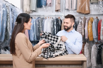 Photo of Dry-cleaning service. Happy worker receiving shirt from client indoors