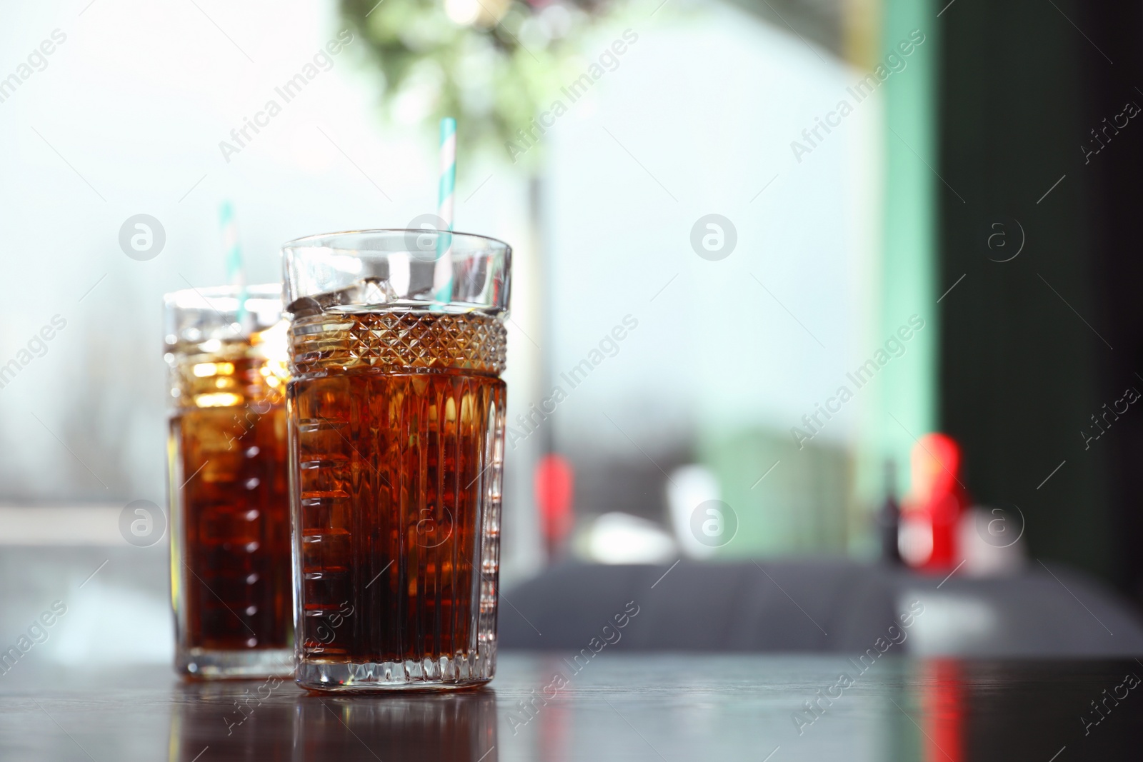 Photo of Glasses with refreshing cola and ice cubes on table indoors. Space for text