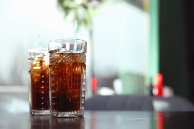 Glasses with refreshing cola and ice cubes on table indoors. Space for text
