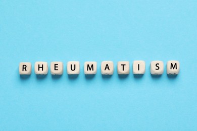 Photo of Word Rheumatism made of cubes on light blue background, top view