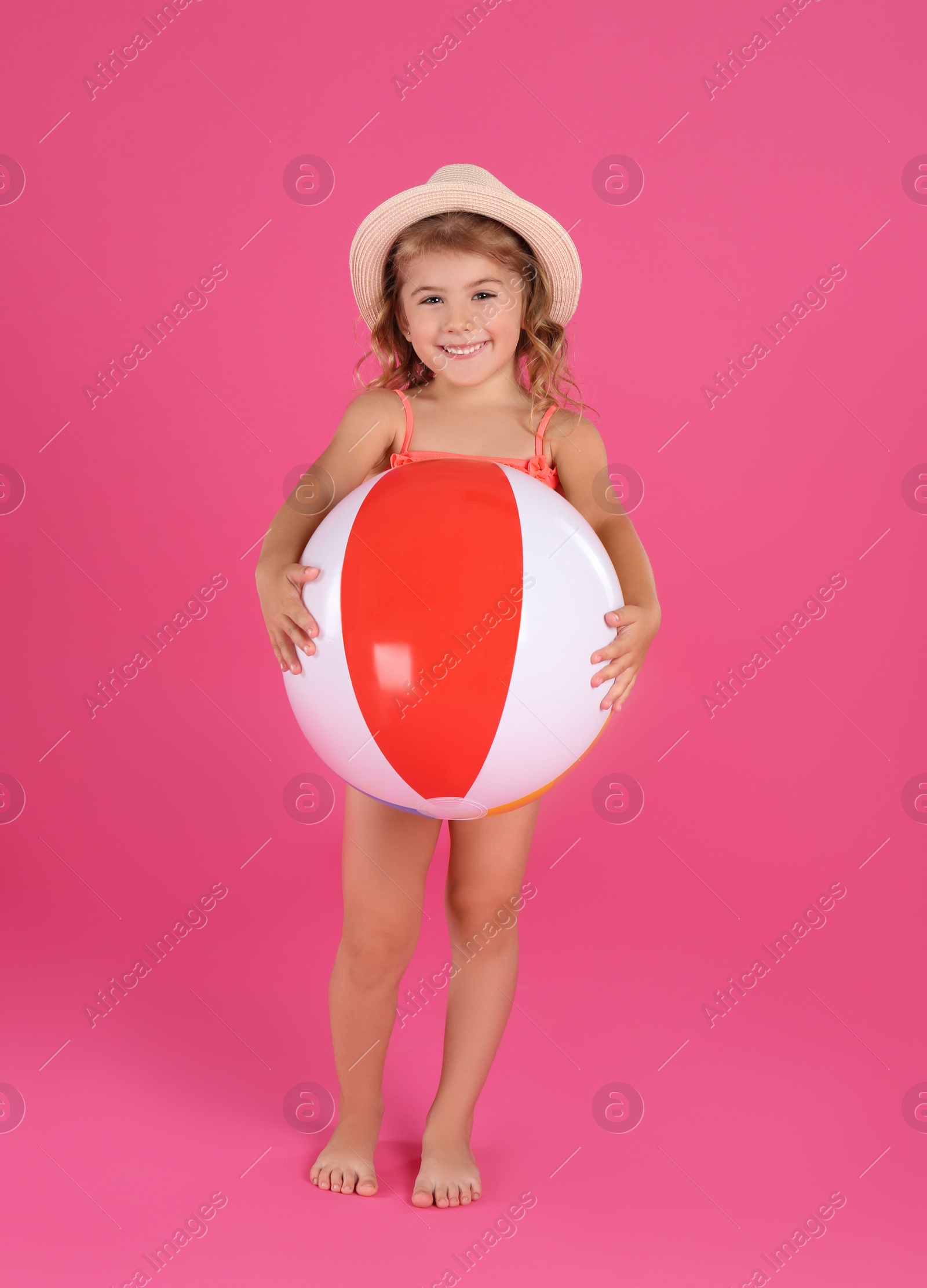 Photo of Cute little child in beachwear with bright inflatable ball on pink background