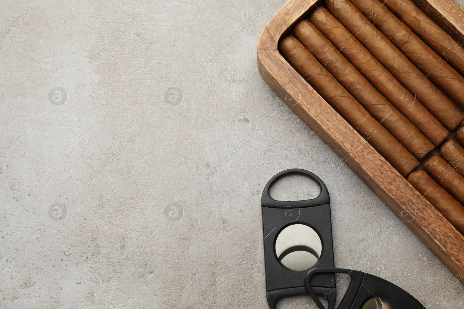 Photo of Box with cigars and guillotine cutters on light grey table, flat lay. Space for text