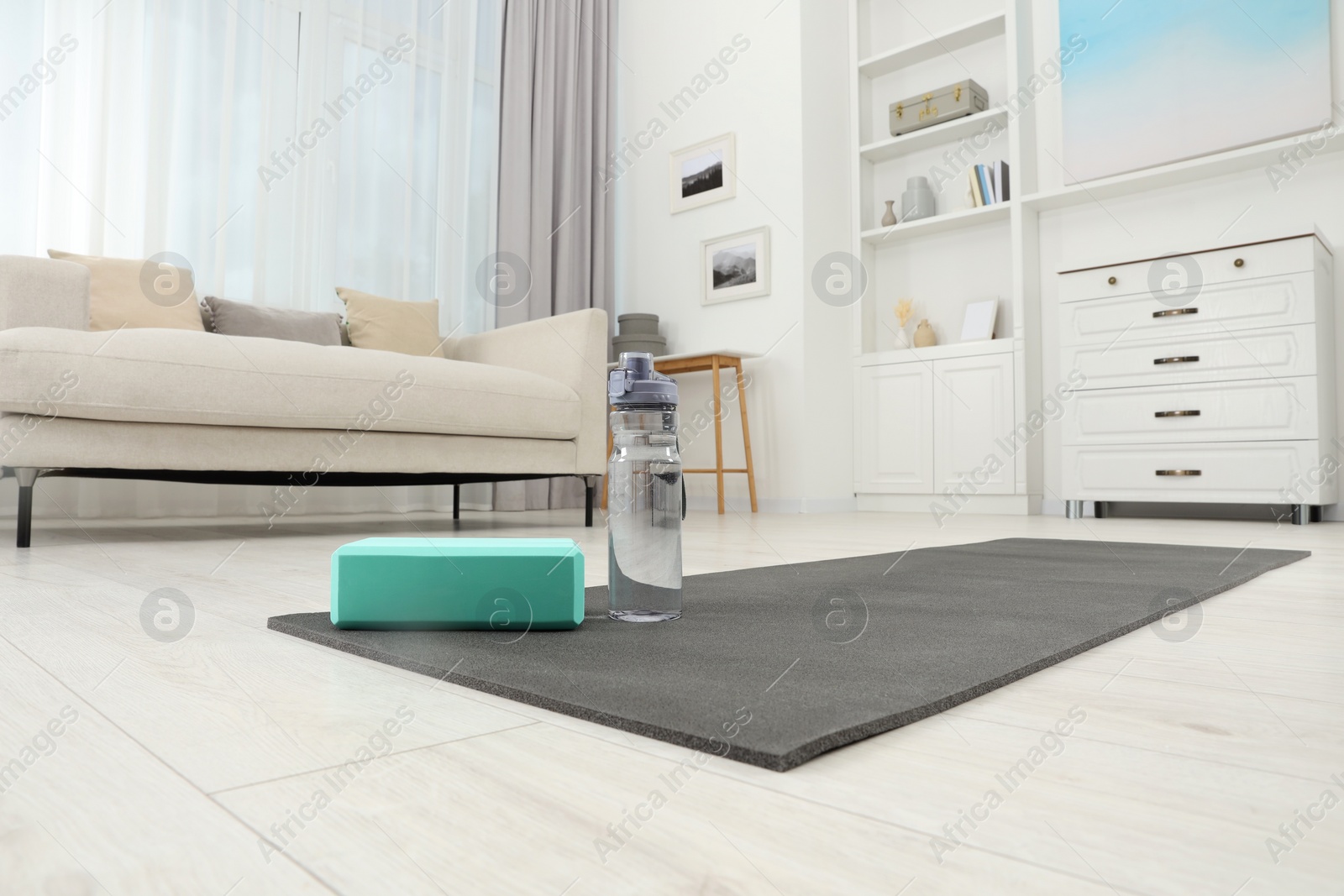 Photo of Exercise mat, yoga block and bottle of water on floor in room