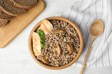 Photo of Tasty buckwheat porridge with meat on white wooden table, flat lay